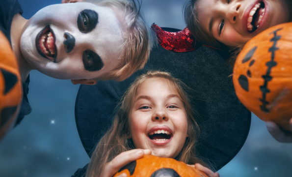 Three children dressed in costume holding pumpkins, looking down at camera