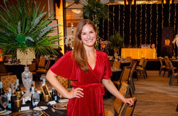 person in red dress smiling in a large empty ballroom