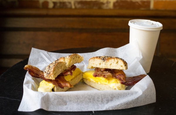 a bacon and egg bagel sandwich and a cup of coffee on a table