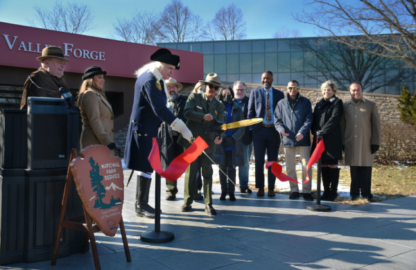 group of people watching a large red ribbon being cut in front of a building