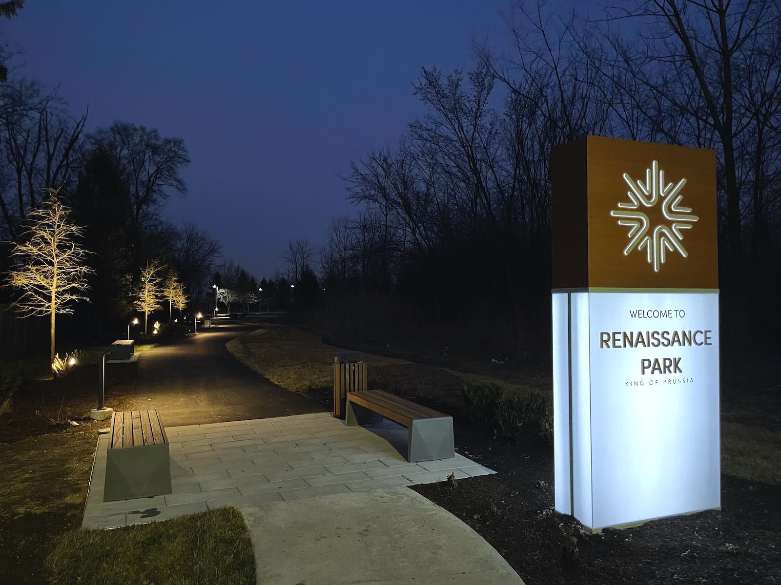 a lit up sign for Renaissance Park outdoors by a trail at night