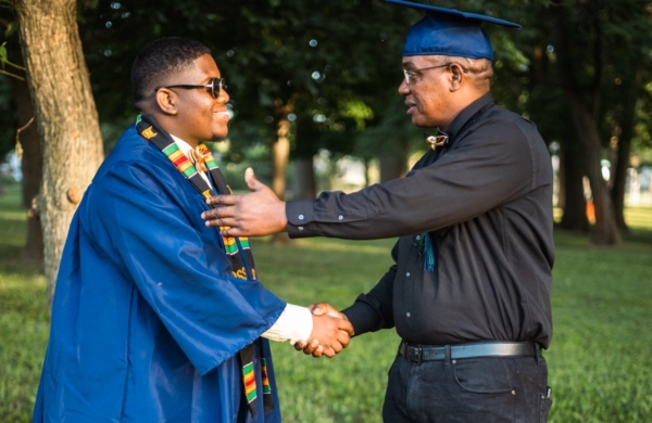 dad shaking son's hand, wearing graduation robe