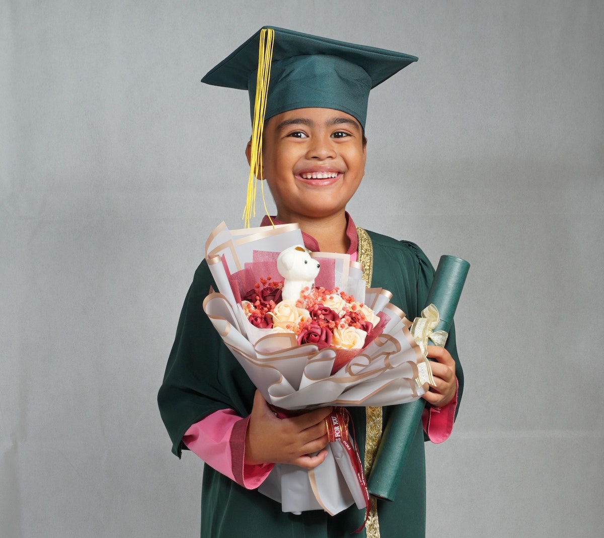 a child in graduation robe and cap holding flowers and diploma