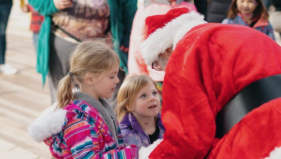 santa leaning over and talking to two small childern
