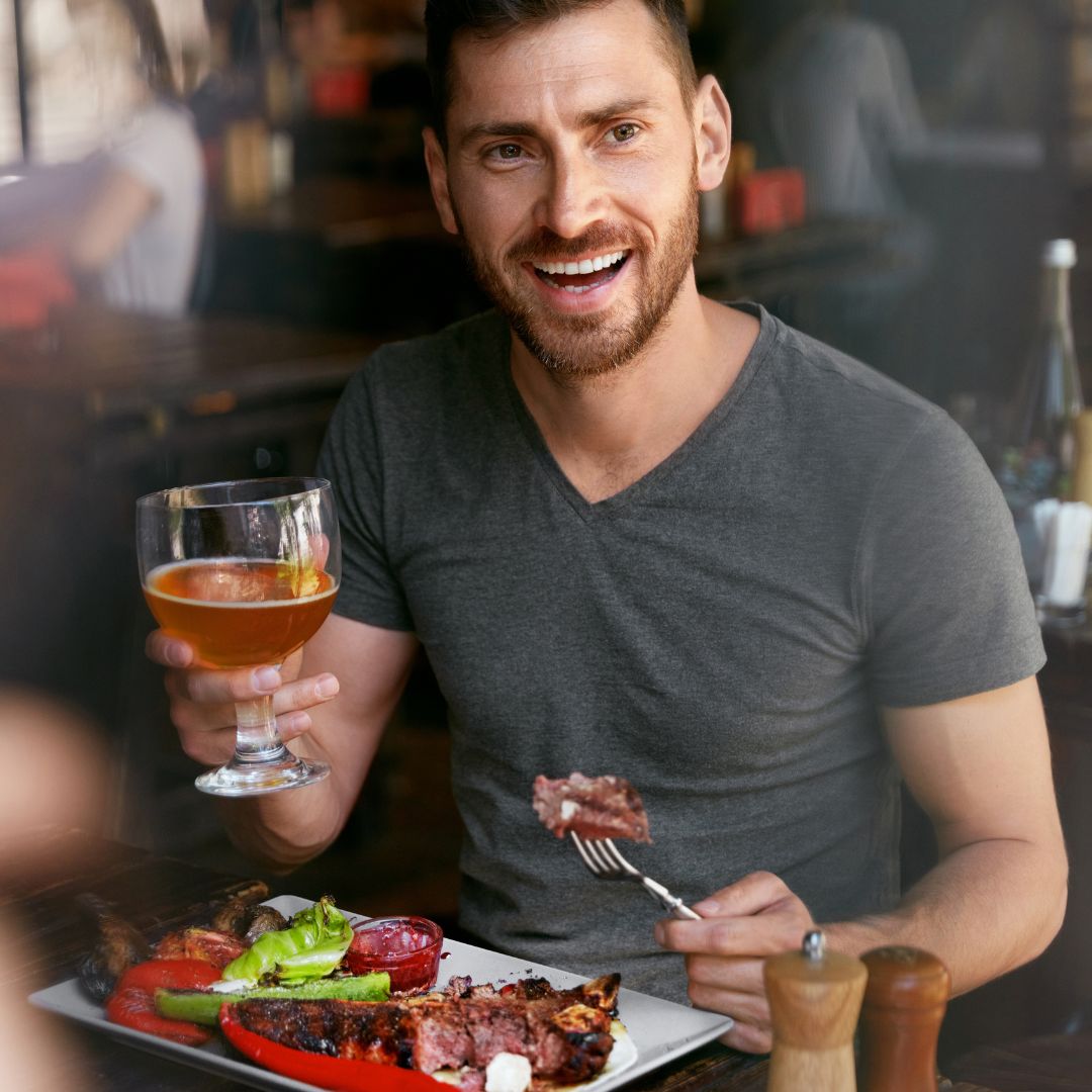person holding a fork with beef on it and holding a drink, smiling